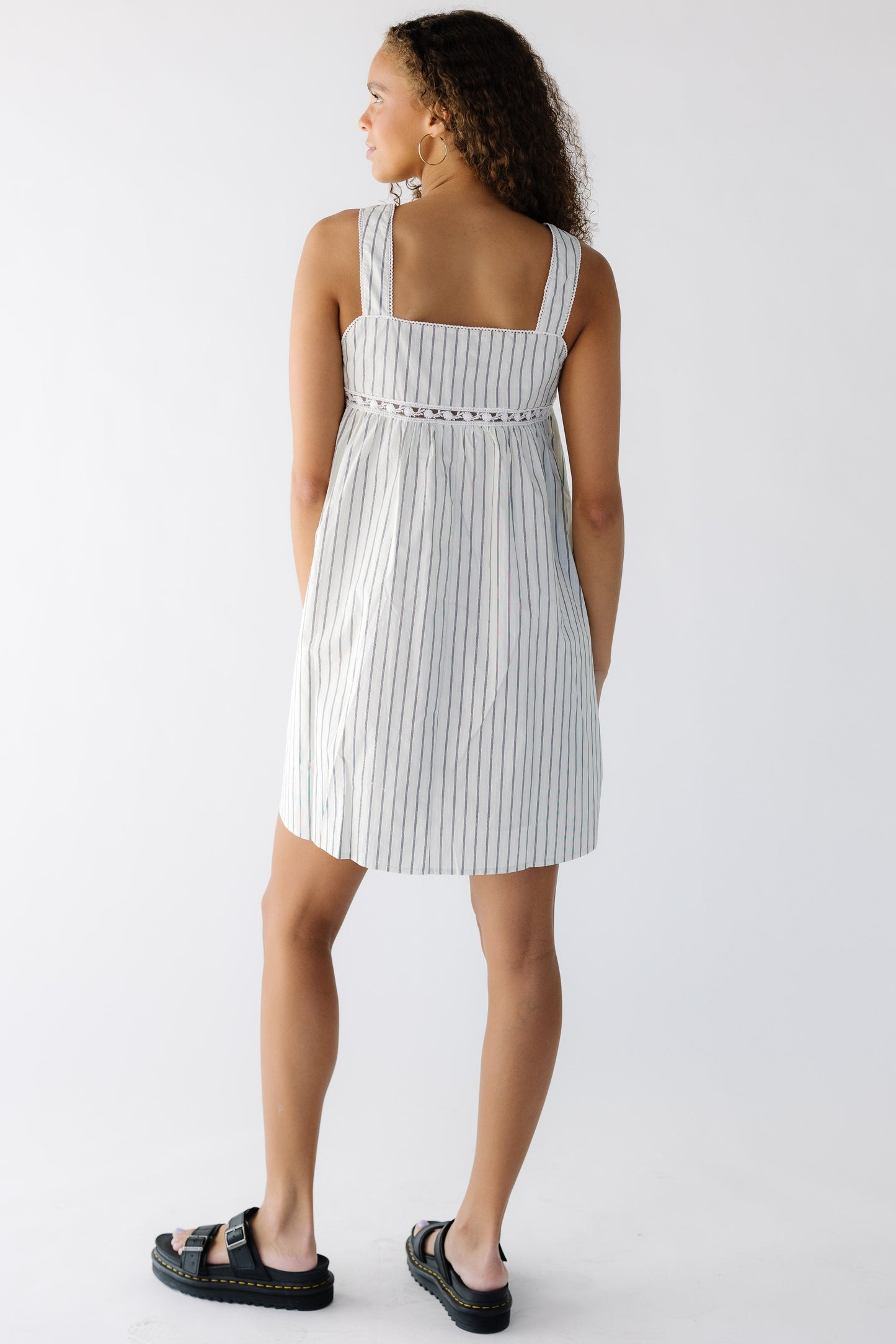 Back view of a teenage girl wearing an off white and black stripe jumper with wide straps and lace inset around the bottom of the bodice.