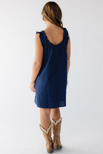 Back view of a young woman wearing a navy texture short dress with a ruffled scoop neckine.