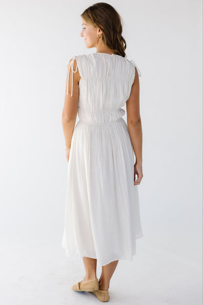 Back view of a woman wearing a sleeveless midi dress in cream with gathered bodice details.