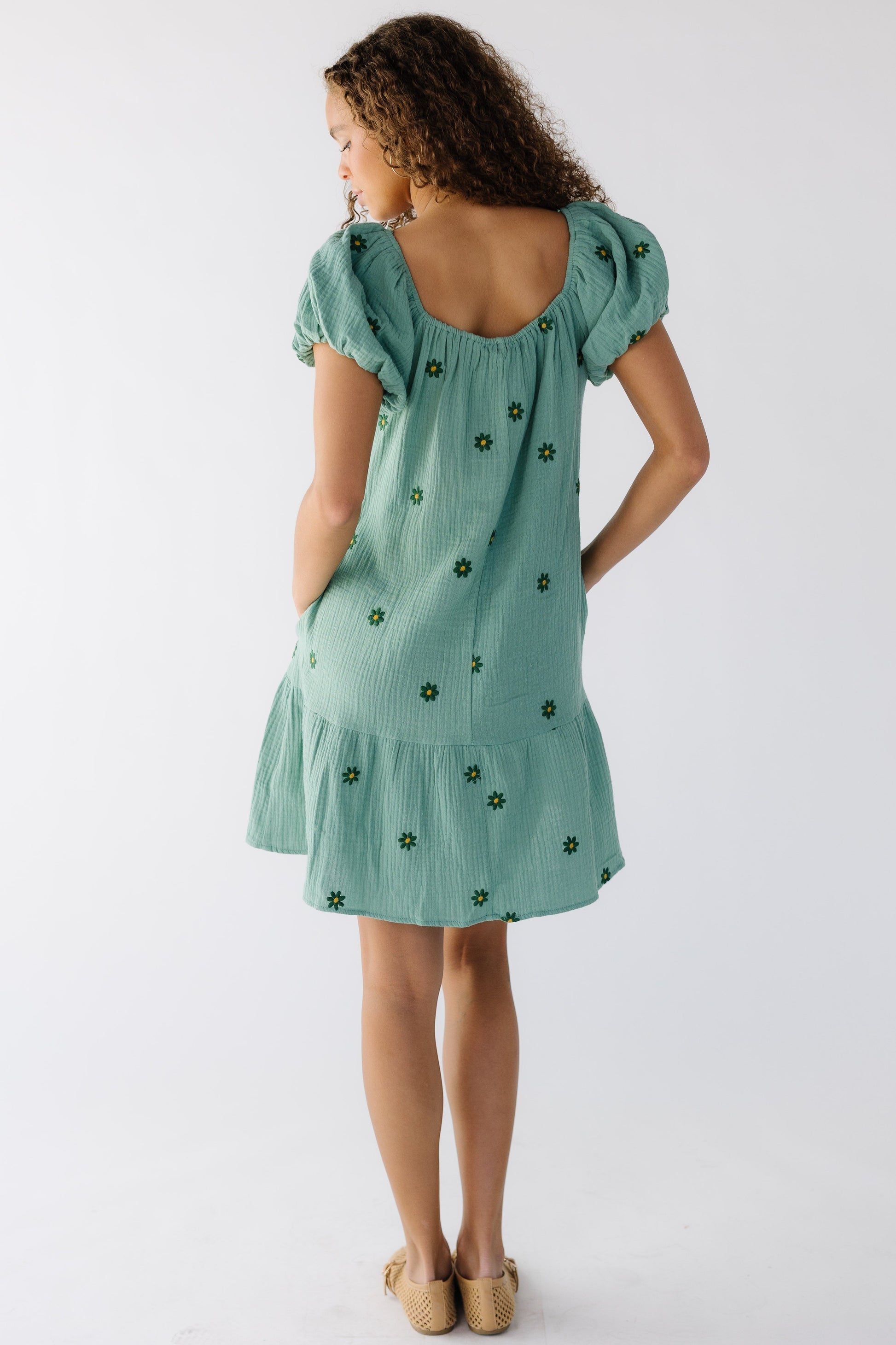 Back view of a teenage girl wearing  loose fitting crepe textured short  dress with a wide bottom ruffle and large puff sleeves.