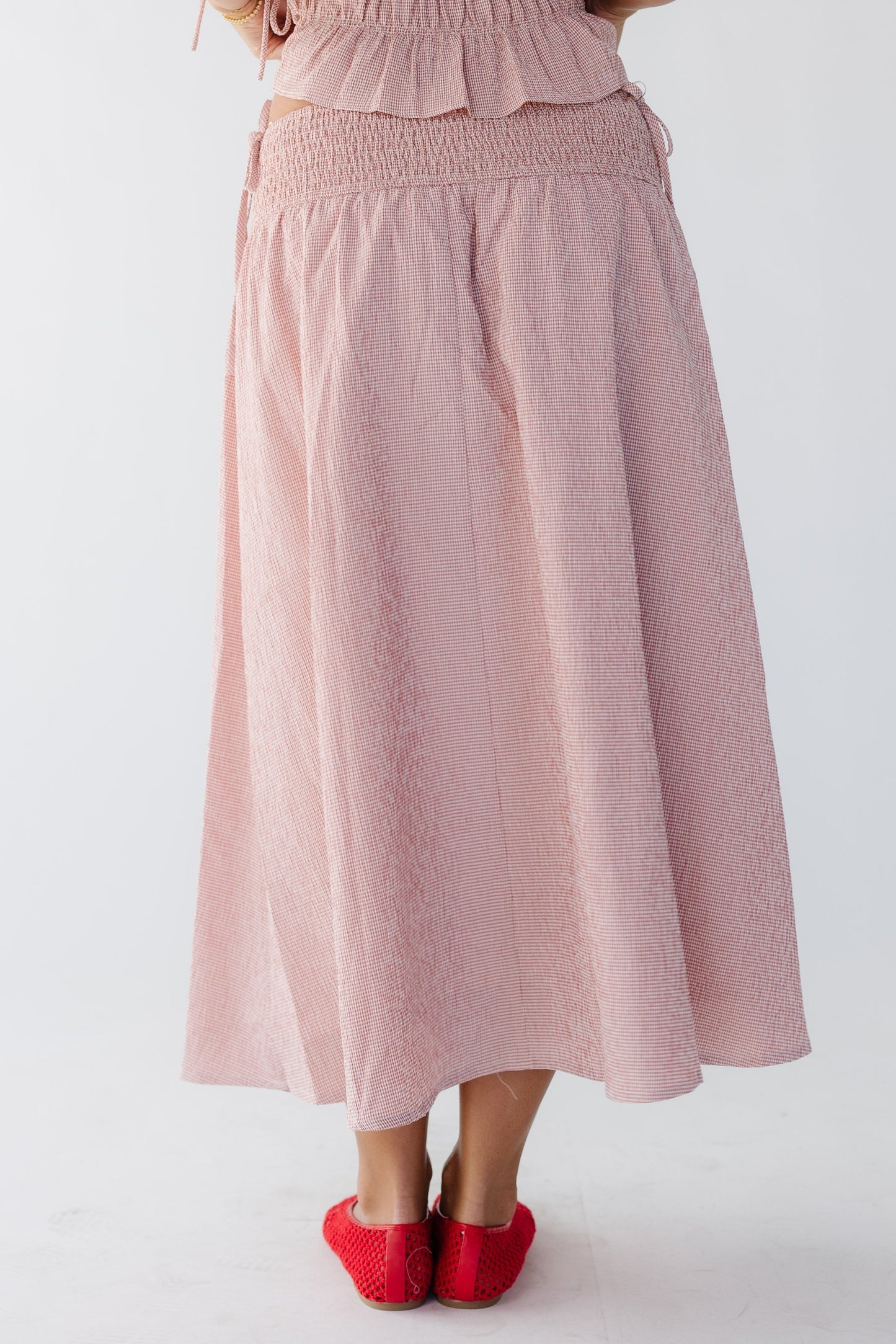Back view of a woman wearing a pink and white midi skirt with a smocked drop waist.