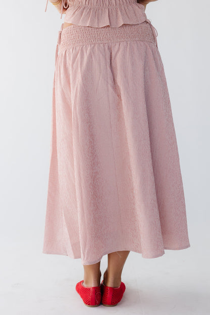 Back view of a woman wearing a pink and white midi skirt with a smocked drop waist.