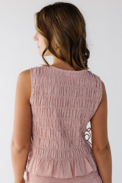Back view of a young woman wearing a pink gingham sleeveless smocked blouse.