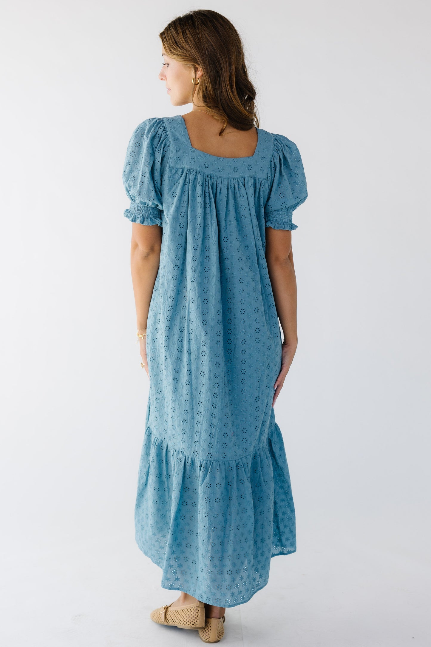 Back view of a woman wearing a loose fitting teal, all eyelet midi dress with a square back neckline and large puff sleeves.