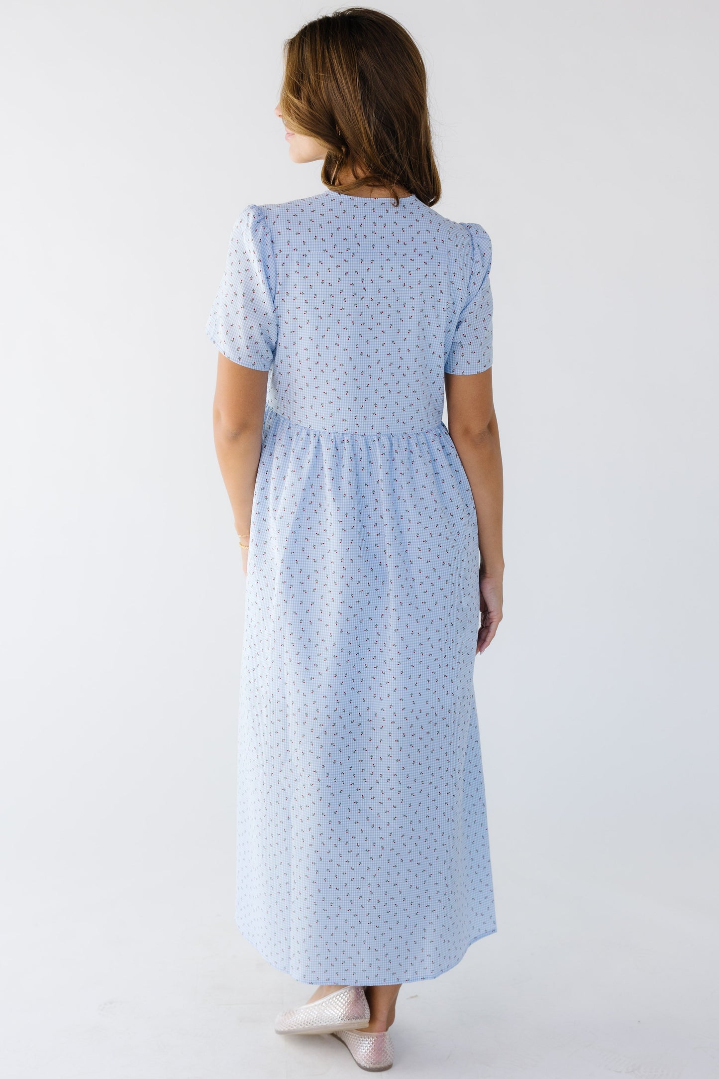 Back view of a young woman wearing a floral & light blue midi dress with short sleeves.