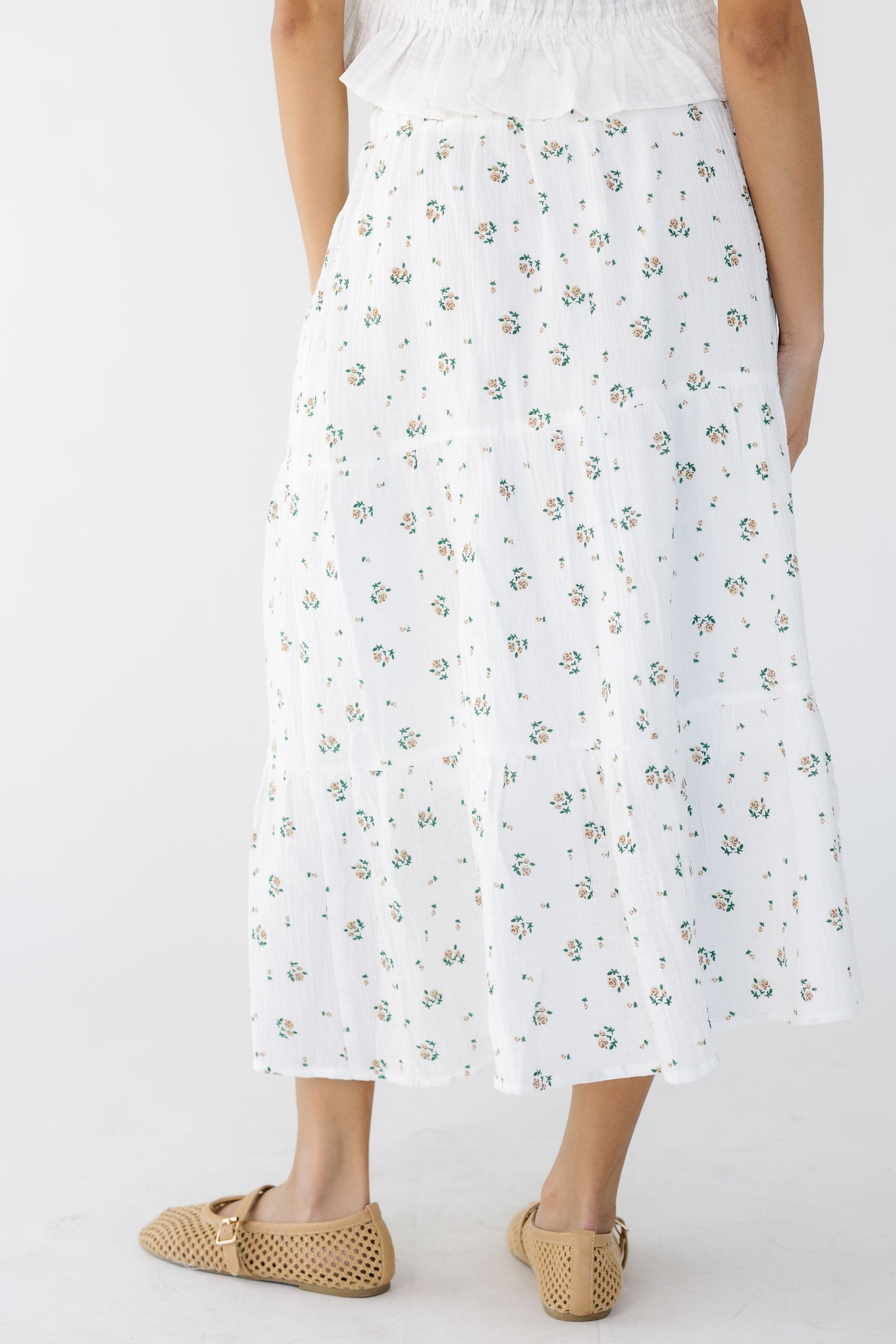 Back view of a woman wearing a white and pink floral print tiered midi skirt.