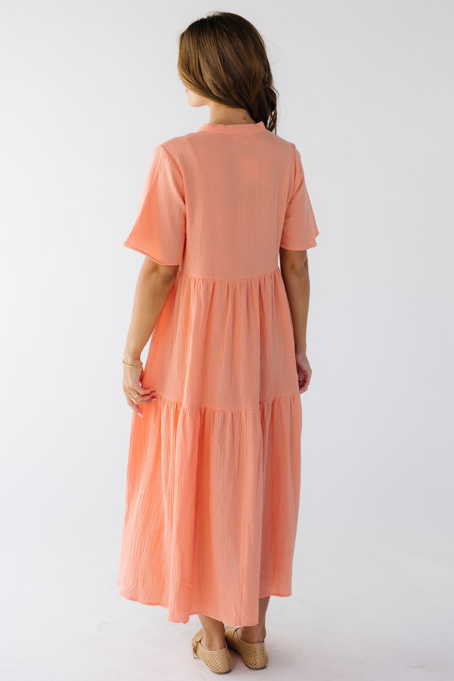 Back view of a young woman wearing a coral loose fitting midi dress with short sleeves.