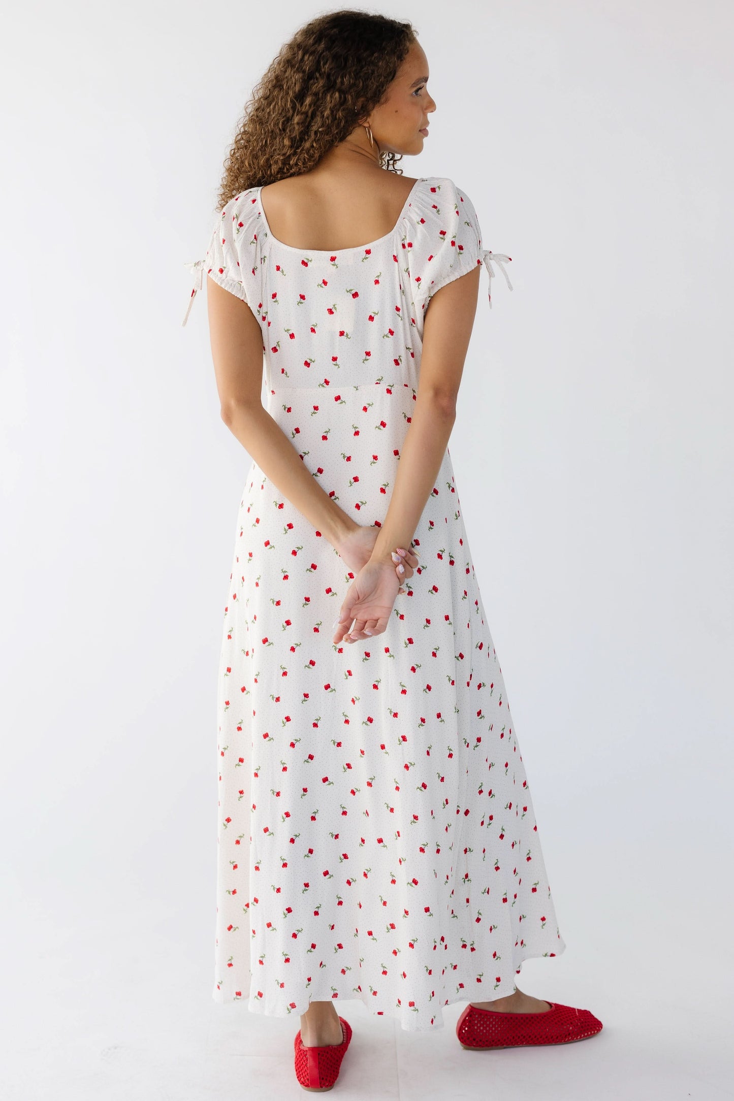 Back view of a teenage girl wearing a closer fitting white floral print midi-maxi  dress with short sleeves and a scoop back neckline.