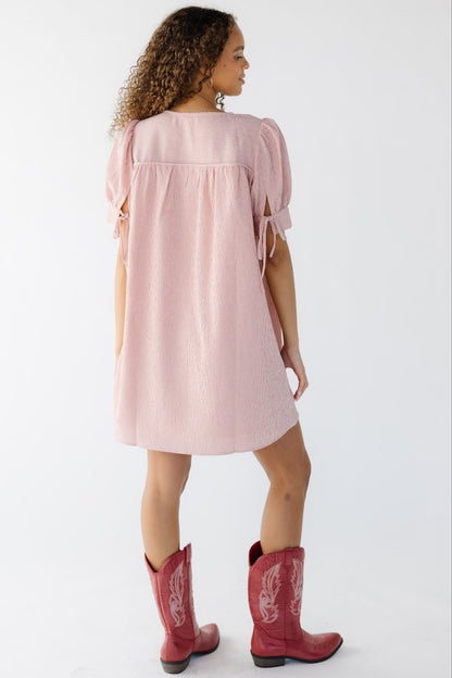 Back view of a woman wearing a pink gingham short dress with short puff sleeves.