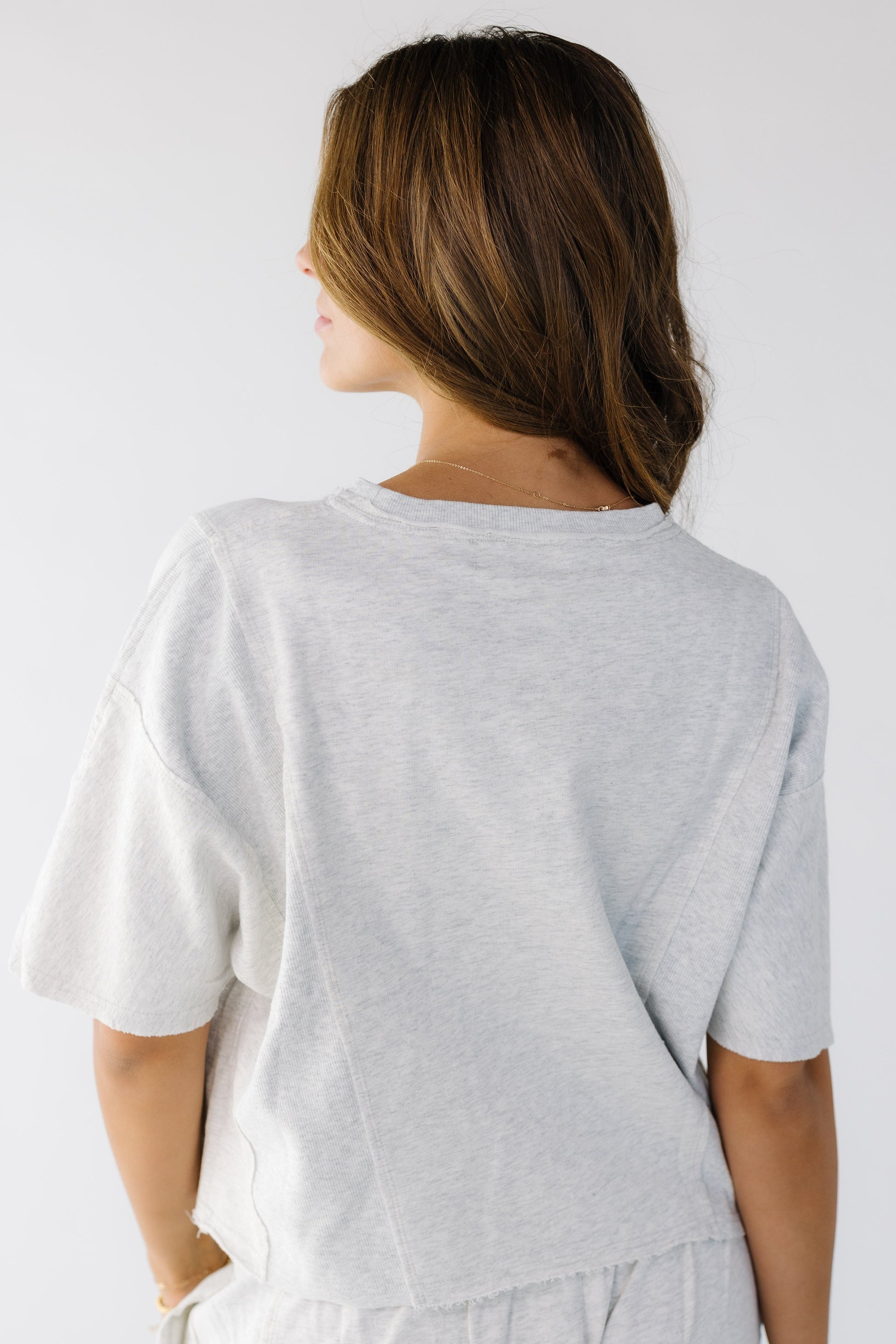 Back view of a young woman wearing a loose fitting tee with rib knit side panels  and elbow length sleeves.