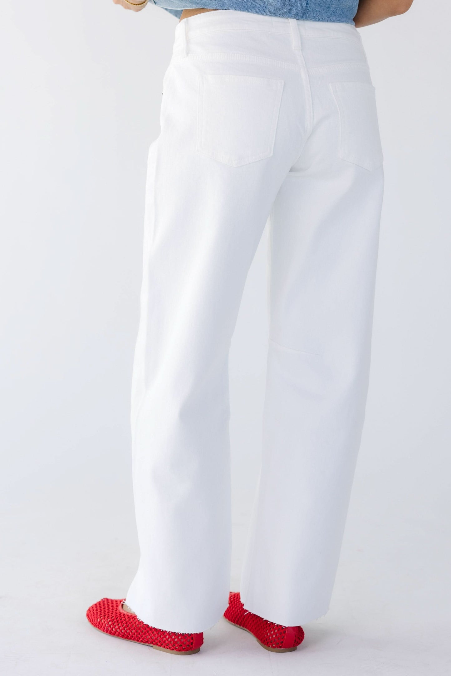 Back view of a young woman wearing white wide leg barrel jeans with scissor cut hems.