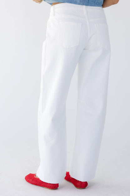 Back view of a young woman wearing white wide leg barrel jeans with scissor cut hems.