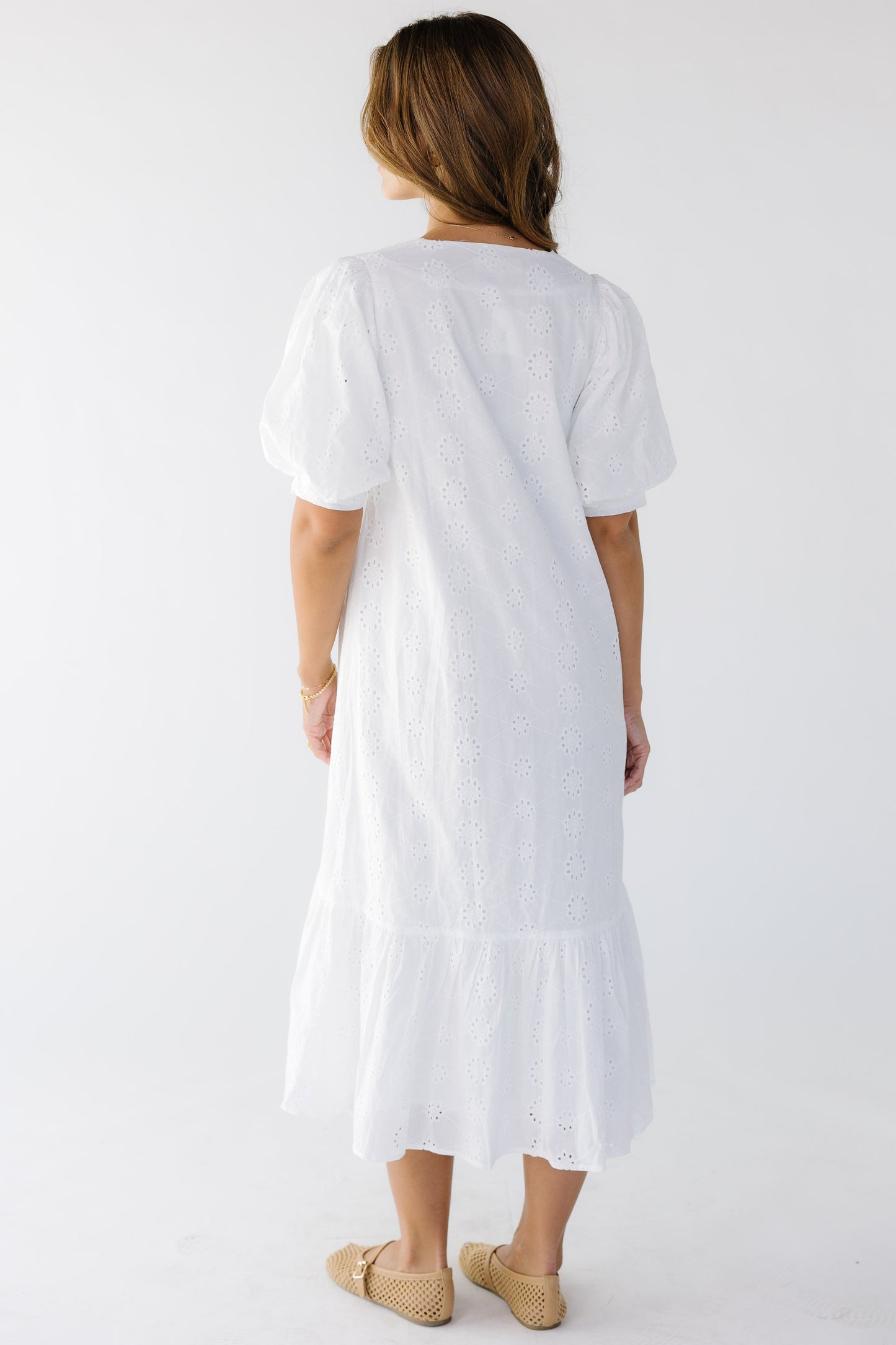 Back view of a woman wearing a white eyelet midi dress with short balloon sleeves.