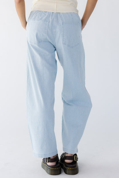 Back view of a young woman wearing a pair of blue & white pinstripe denim wide leg pants with back pockets.