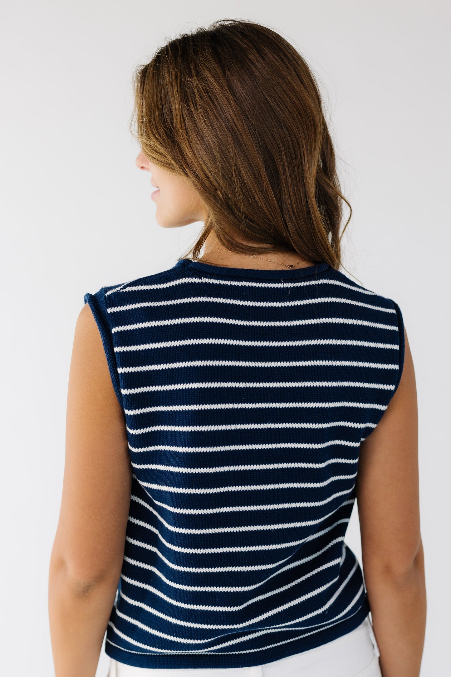 Back view of a woman wearing a navy and white stripe sweater vest with a round neckline.