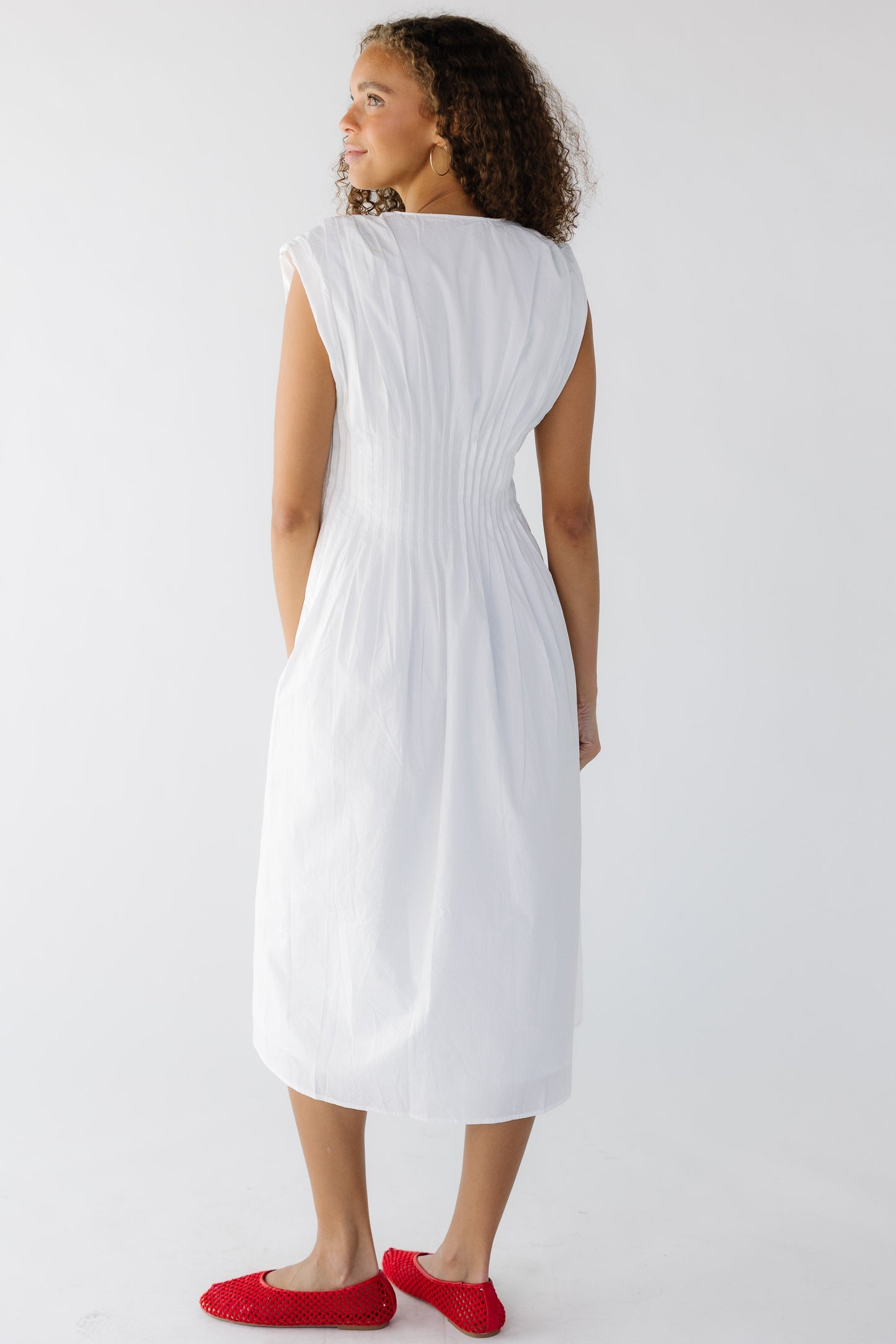 Back view of a teen girl wearing a white sleeveless midi dress with a closer fitting waist and a full skirt.
