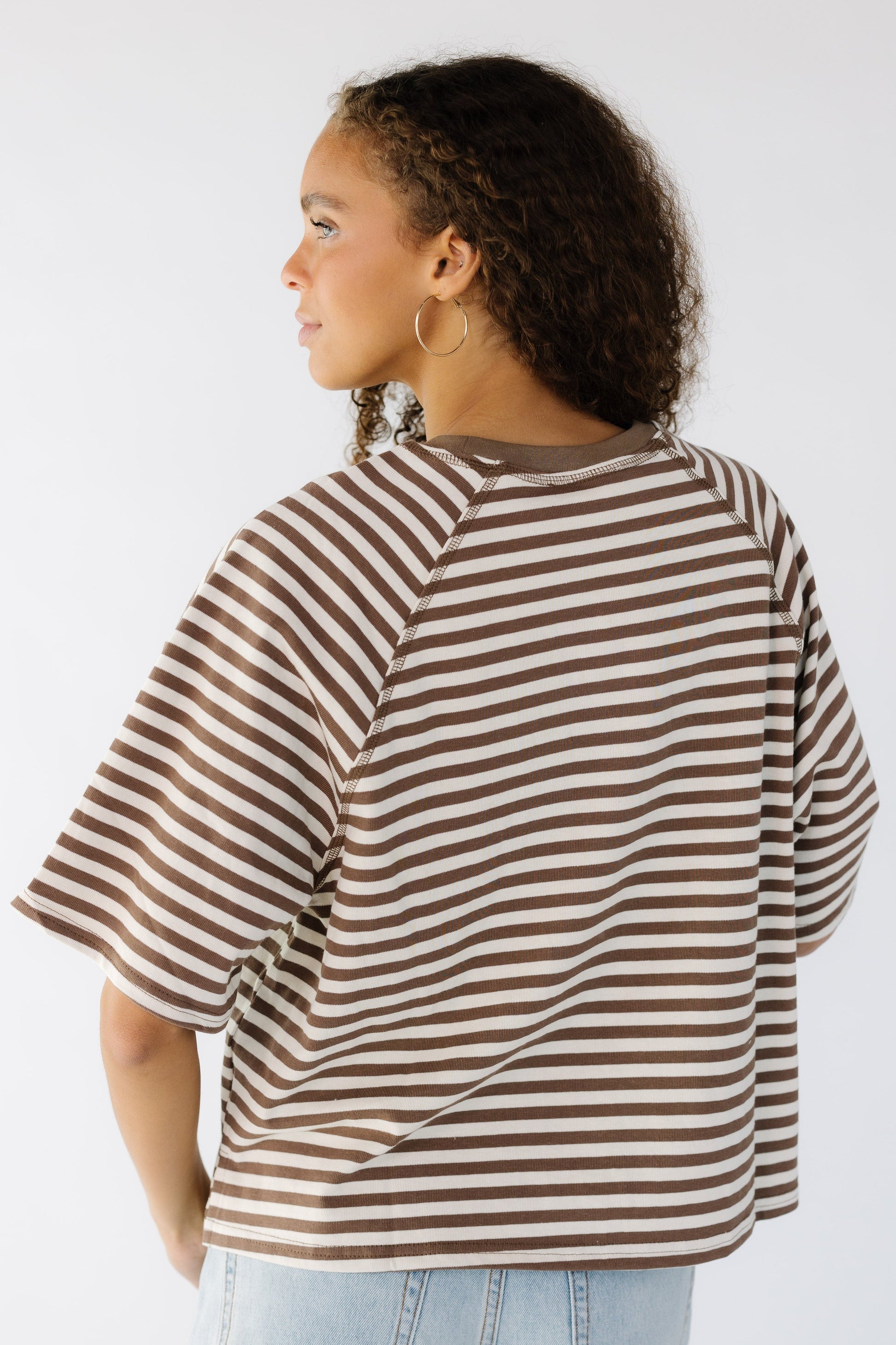 Back view of a teen girl wearing a brown and white stripe, loose fitting tee.