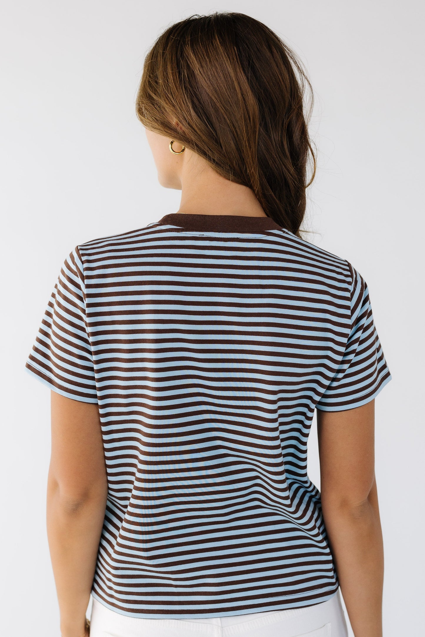 Back view of a woman wearing a short sleeve brown and blue stripe tee.