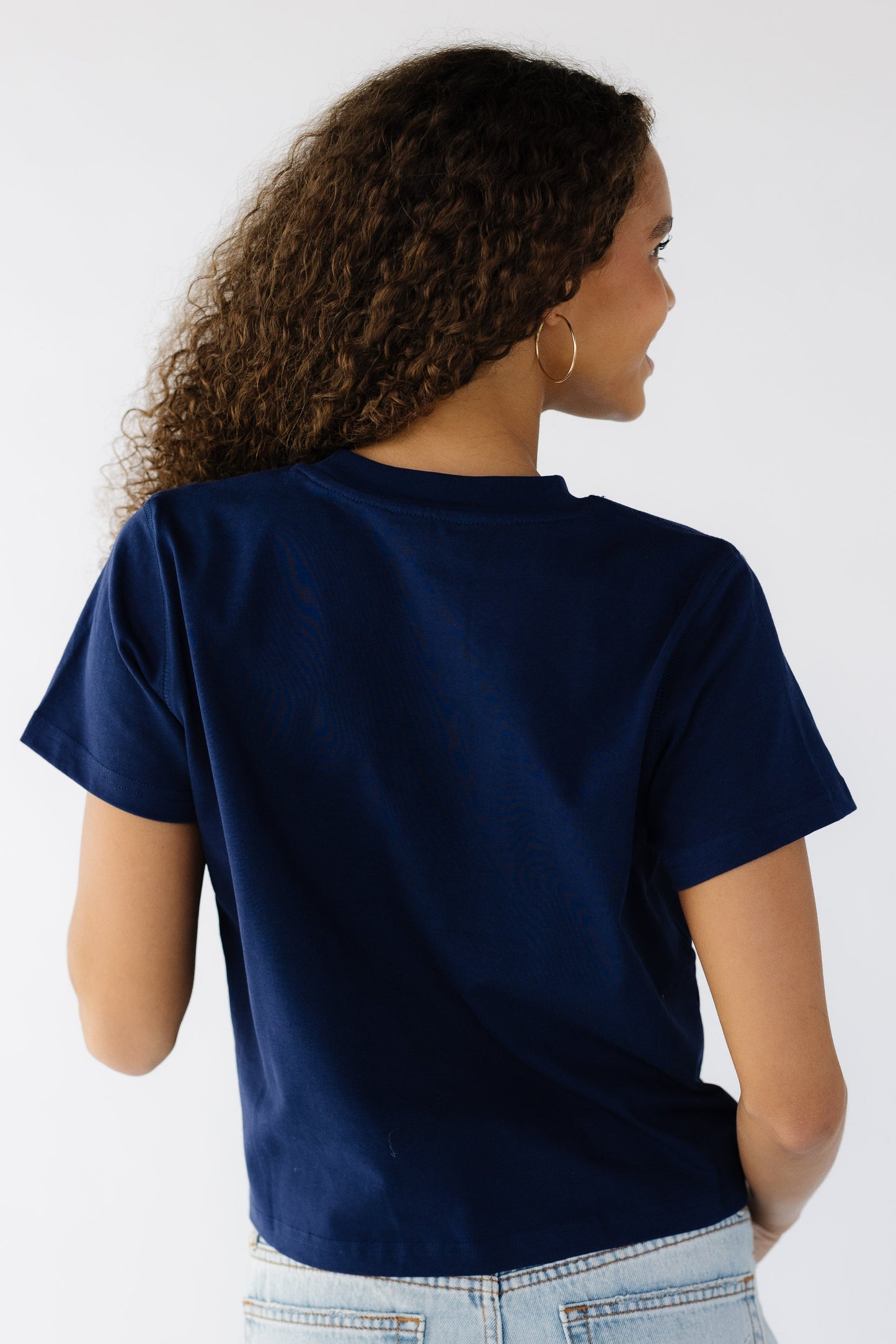 Back view of a teen girl wearing a short sleeve navy tee.