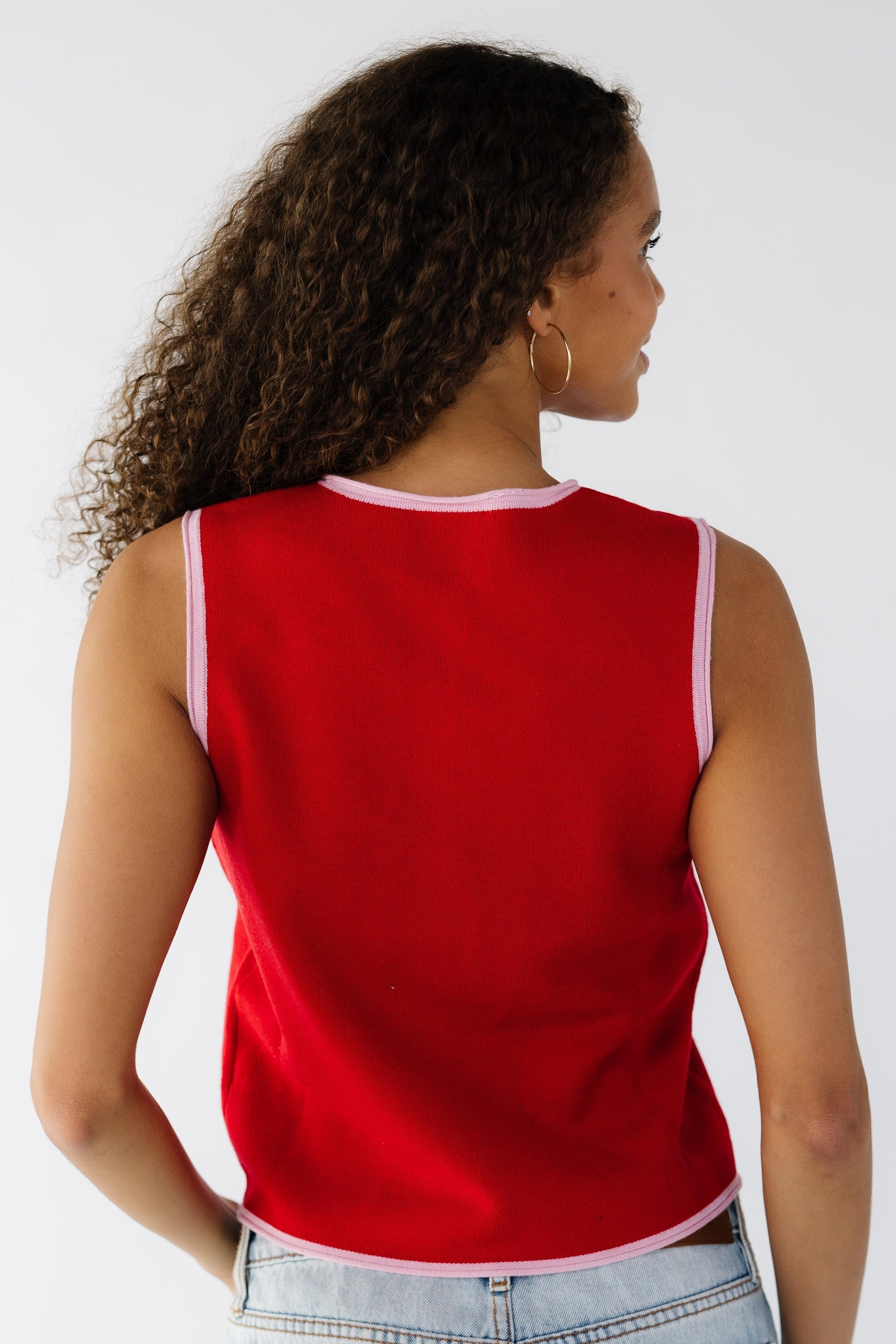 Back view of a teen girl wearing a red sleeveless top with pink trim hems.