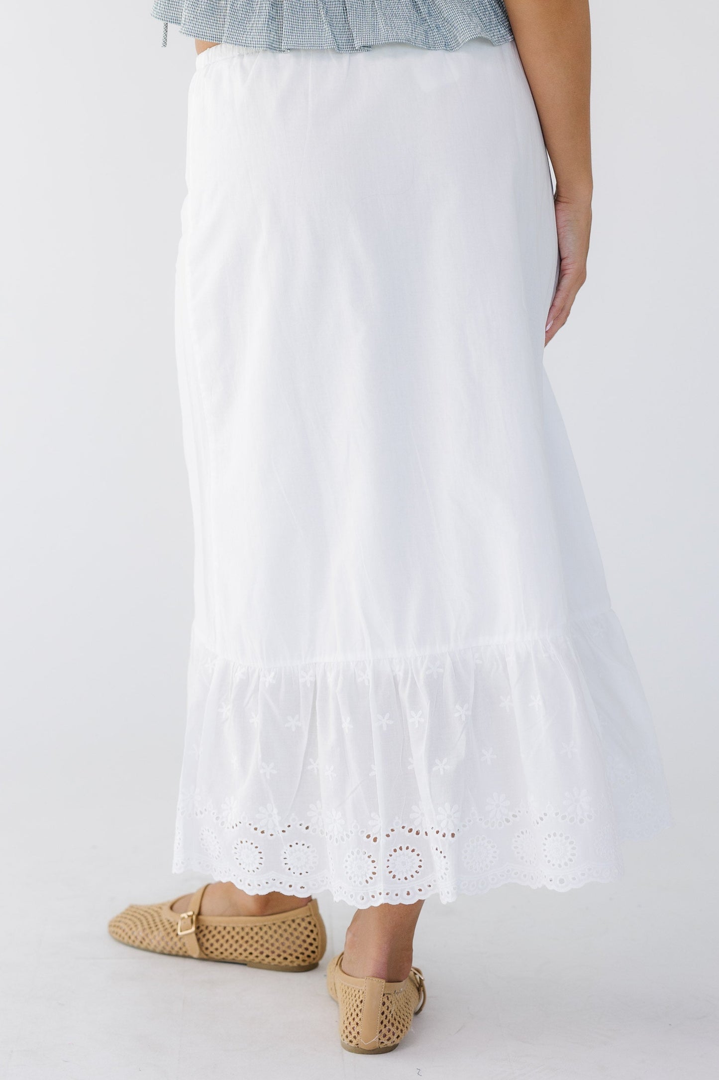 back view of a young woman wearing a white A-line midi skirt with wide bottom eyelet ruffle.
