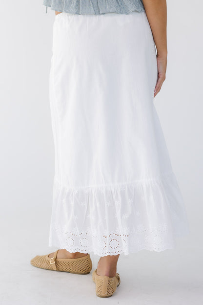back view of a young woman wearing a white A-line midi skirt with wide bottom eyelet ruffle.