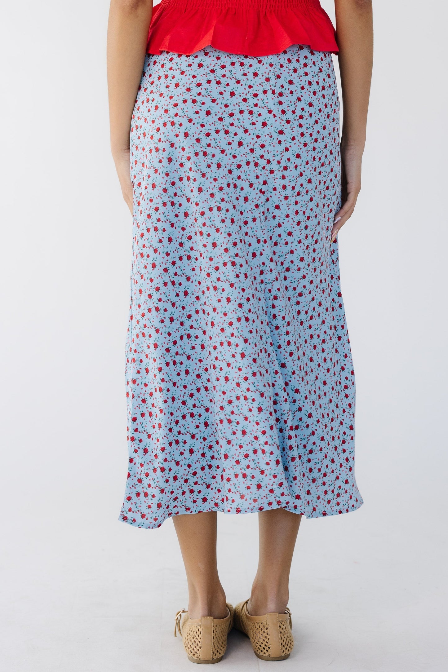 Back view of a woman wearing a light blue A-line midi skirt with a red floral print.