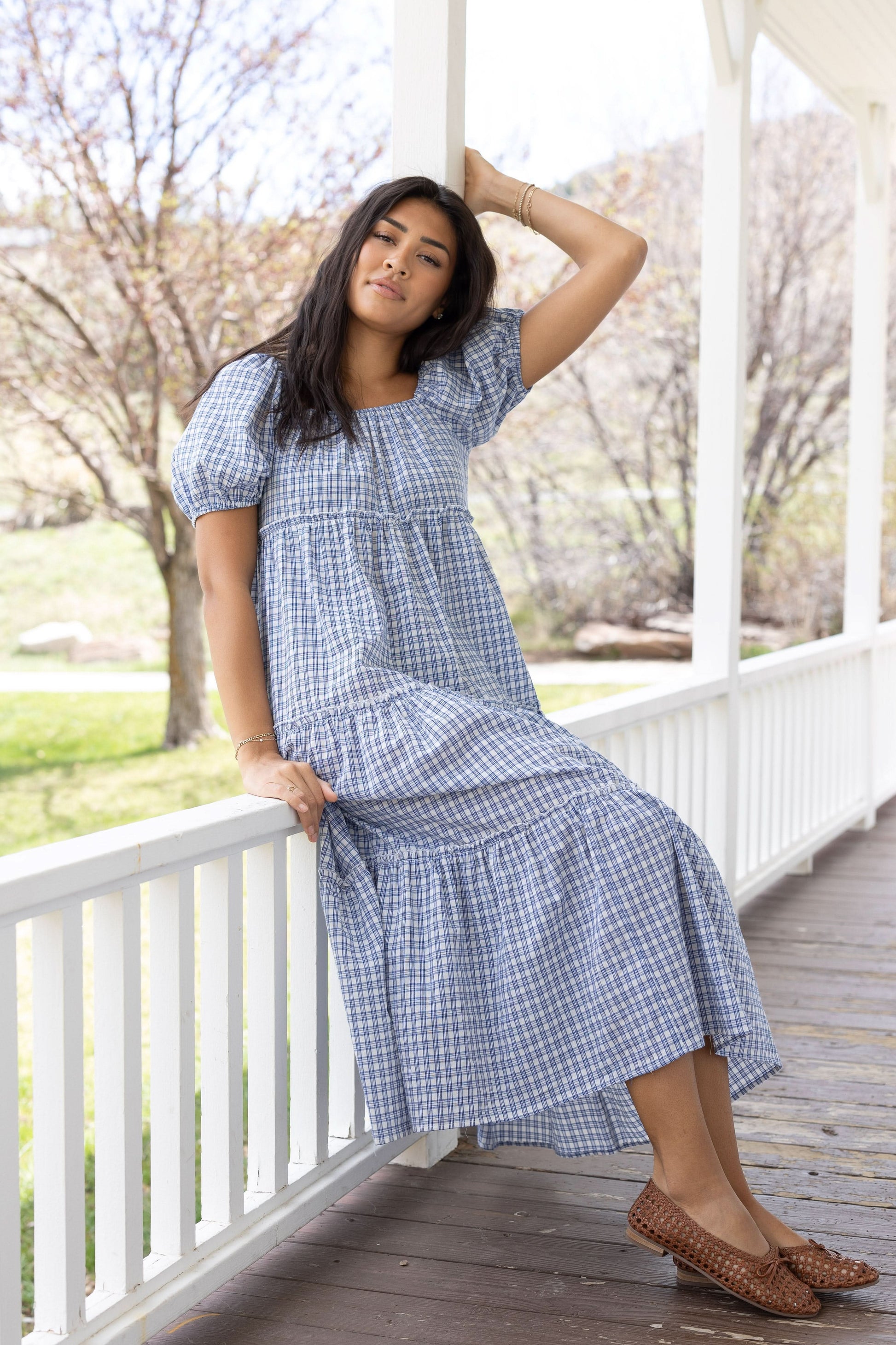 Young woman wearing a modest blue and white plaid tiered midi dress with an elastic square neckline and balloon sleeves.