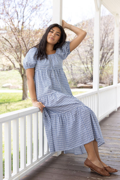 Young woman wearing a modest blue and white plaid tiered midi dress with an elastic square neckline and balloon sleeves.