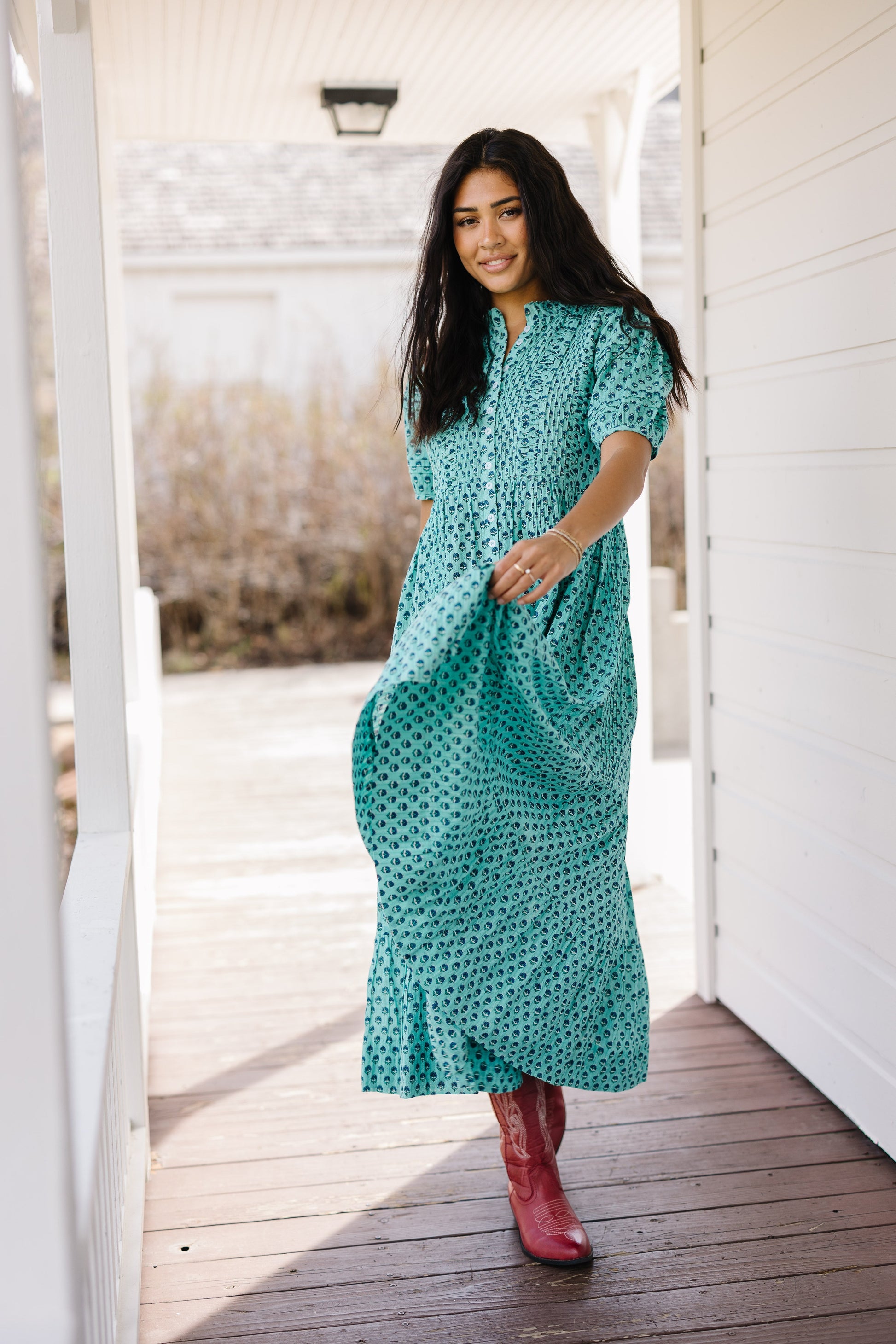 Young woman wearing a teal print button down midi dress wtih pleat andruching details, short sleeves and a round neckline.