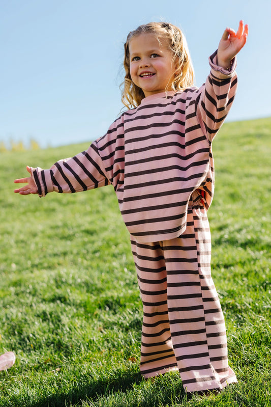 Little girl wearing a loose fitting lounge set in pink and brown stripe with wide leg pants.