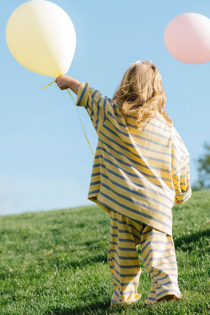 Back view of a little girl wearing a yellow & blue stripe loose fitting lounge set.