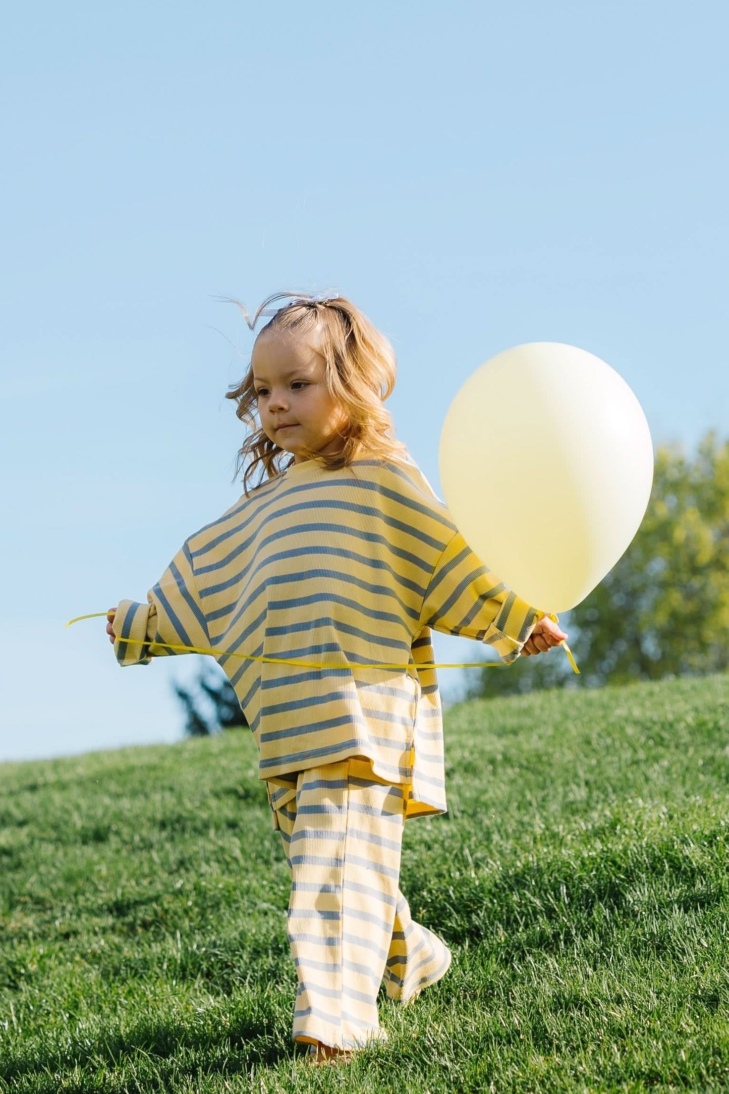 Little girl wearing a yellow & blue stripe lounge set with wide cut leg and long sleeves.