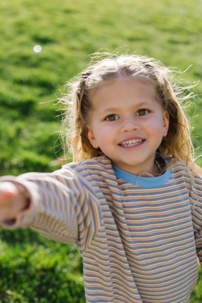 Little girl wearing a loose fitting lounge set in a 3 color stripe with long sleeves and a crew neckline.