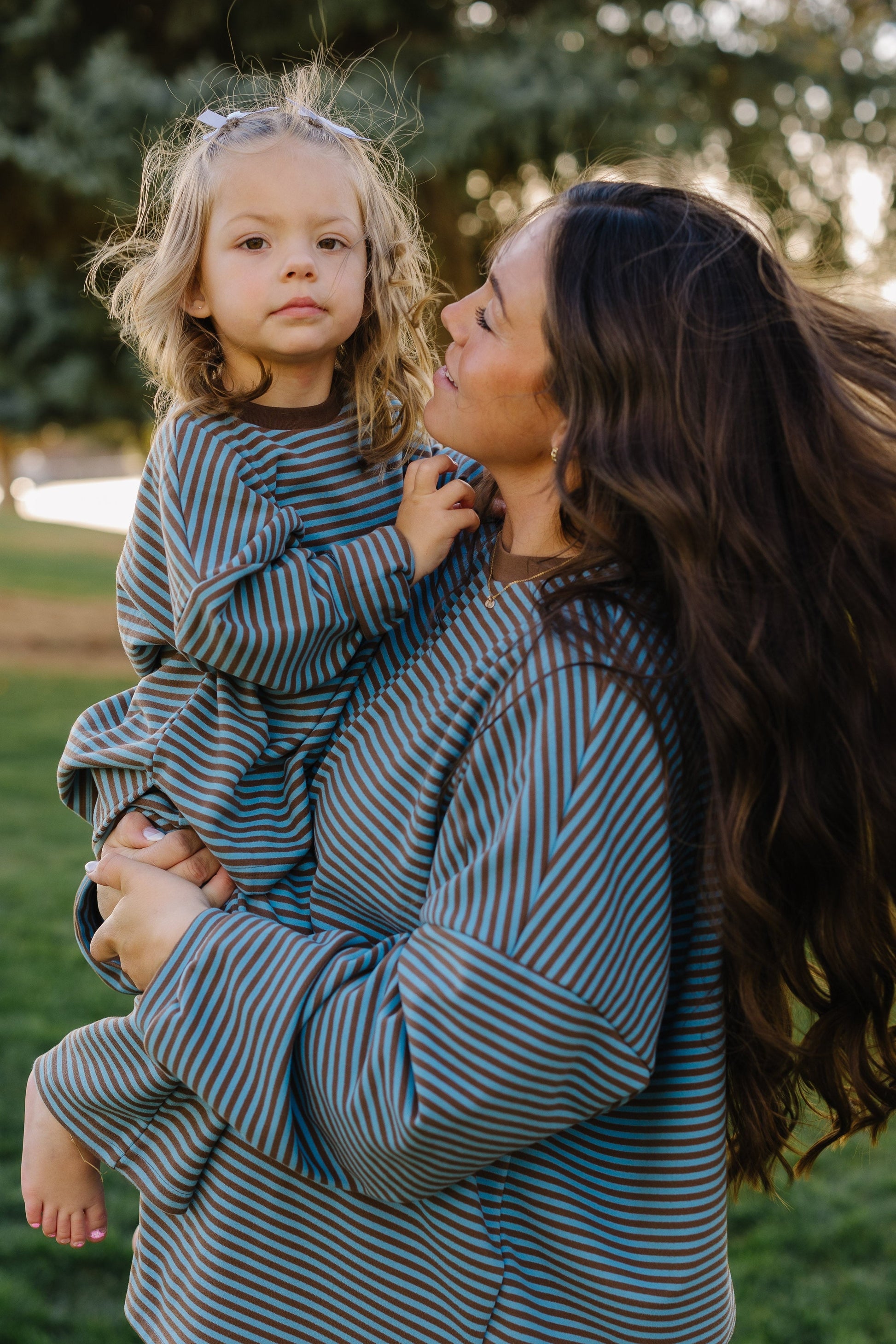 Adult and little girl wearing matching lounge sets in blue and brown with long sleeves and a crew neckline.