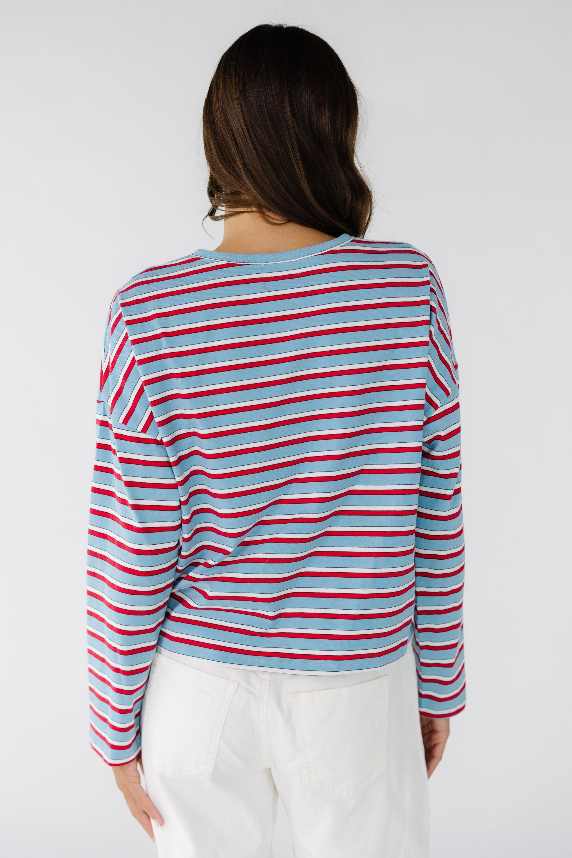 Back view of a woman wearing a long sleeve jersey cardigan in  light blue, red & white.