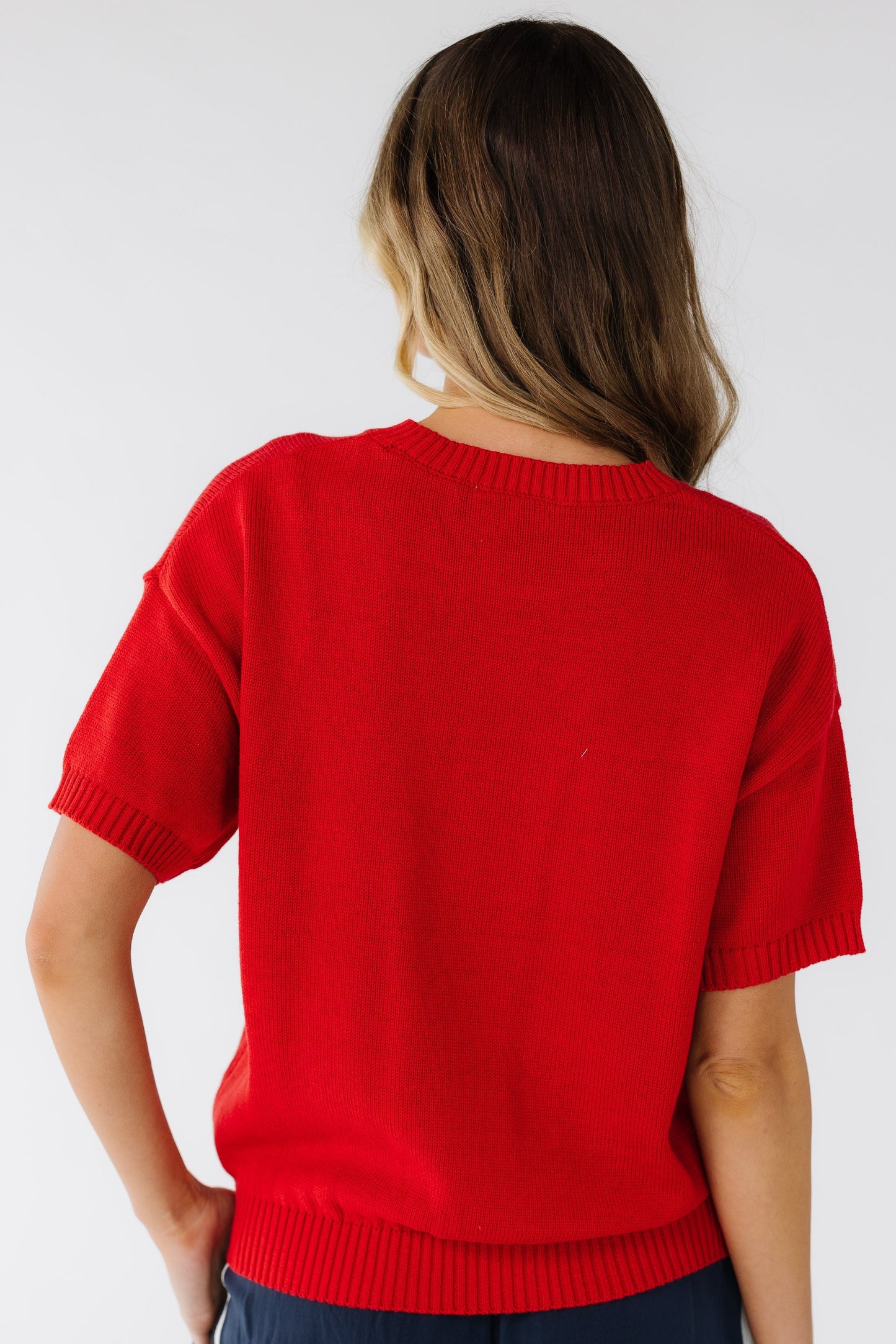 Back view of a young woman wearing a red short sleeve sweater with a ribbed waist.