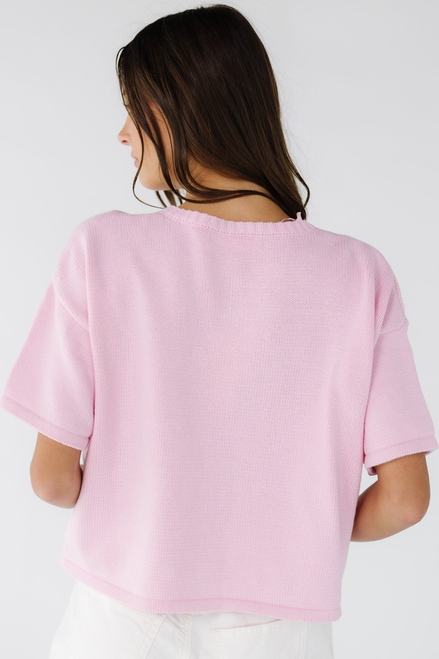 Back view of a woman wearing a pink short sleeve sweater.