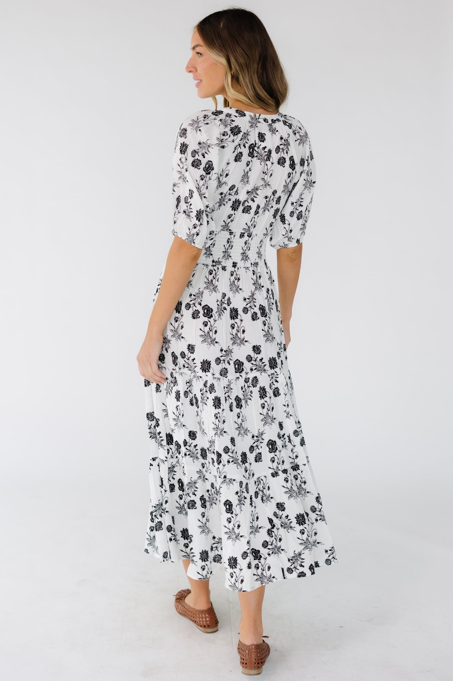 Back view of a young woman wearing a white with black floral print  and elbow length sleeves.