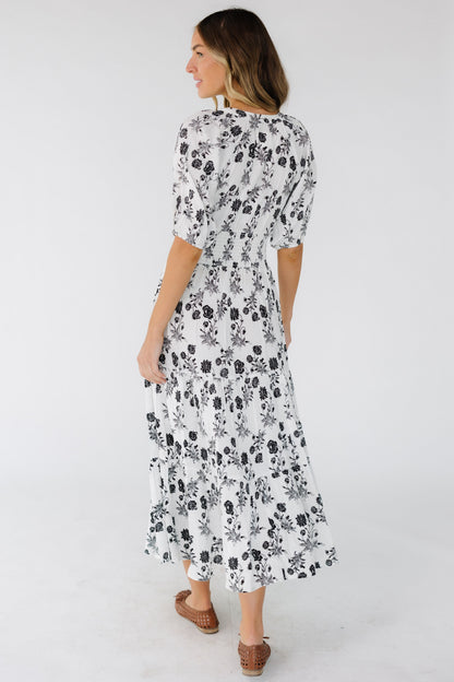 Back view of a young woman wearing a white with black floral print  and elbow length sleeves.