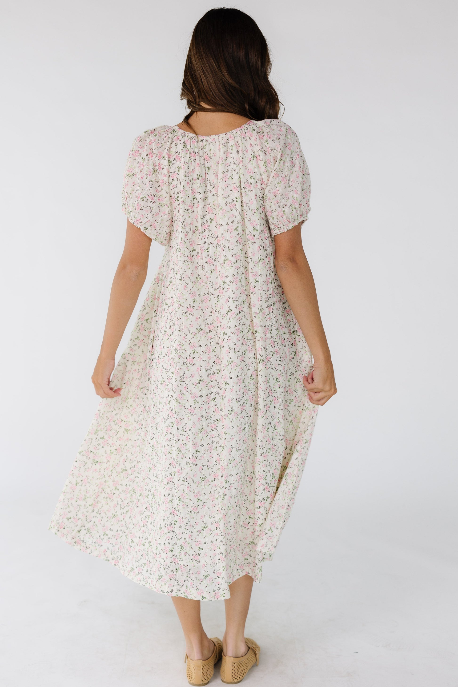 Back view of a woman wearing a white with pink floral print midi dress with balloon sleeves.