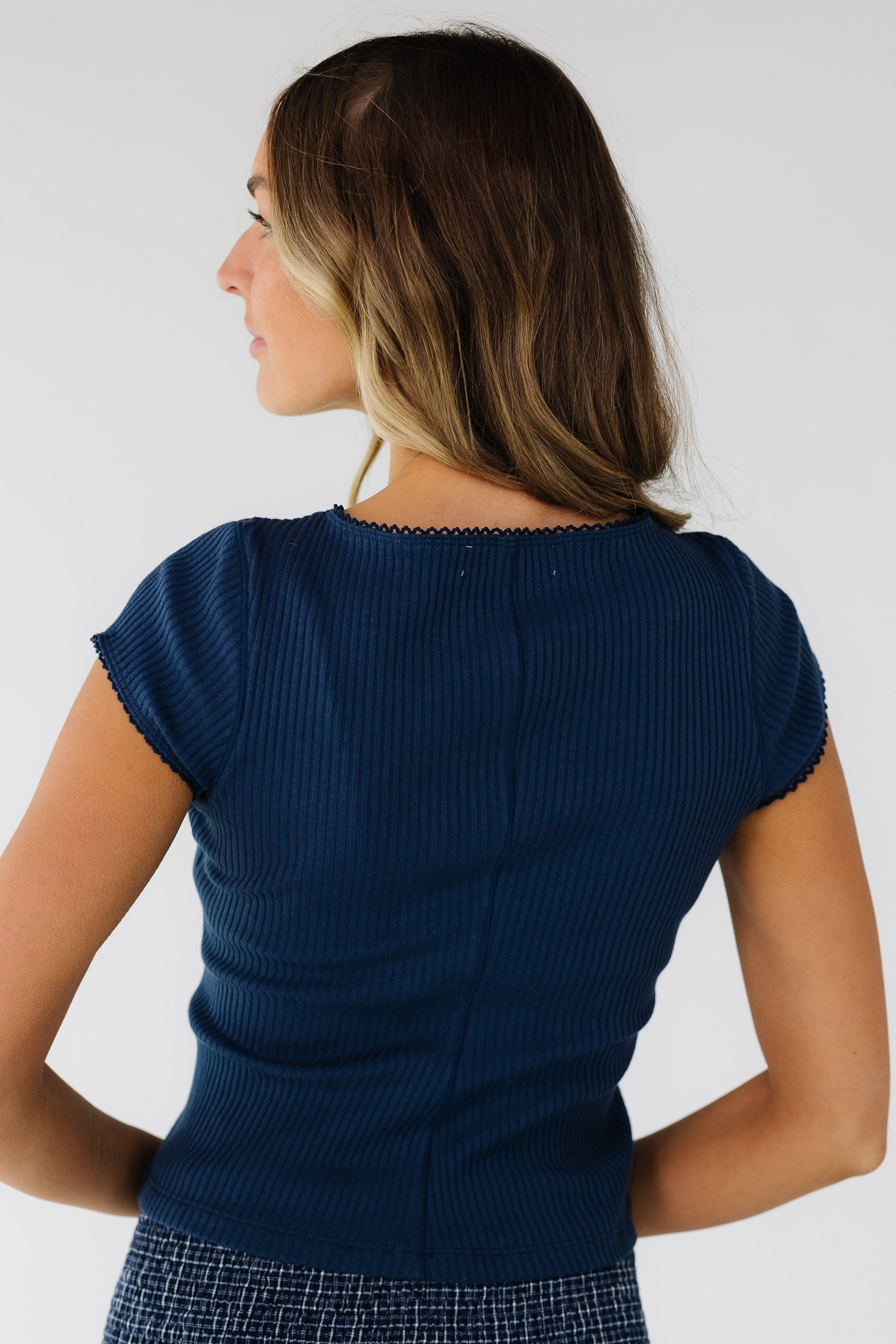 Back view of a woman wearing a close fitting navy rib knit top.