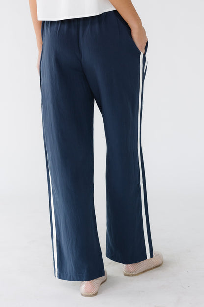 Back view of a woman wearing a pair of navy wide leg track pant with side pockets and an elastic waist.