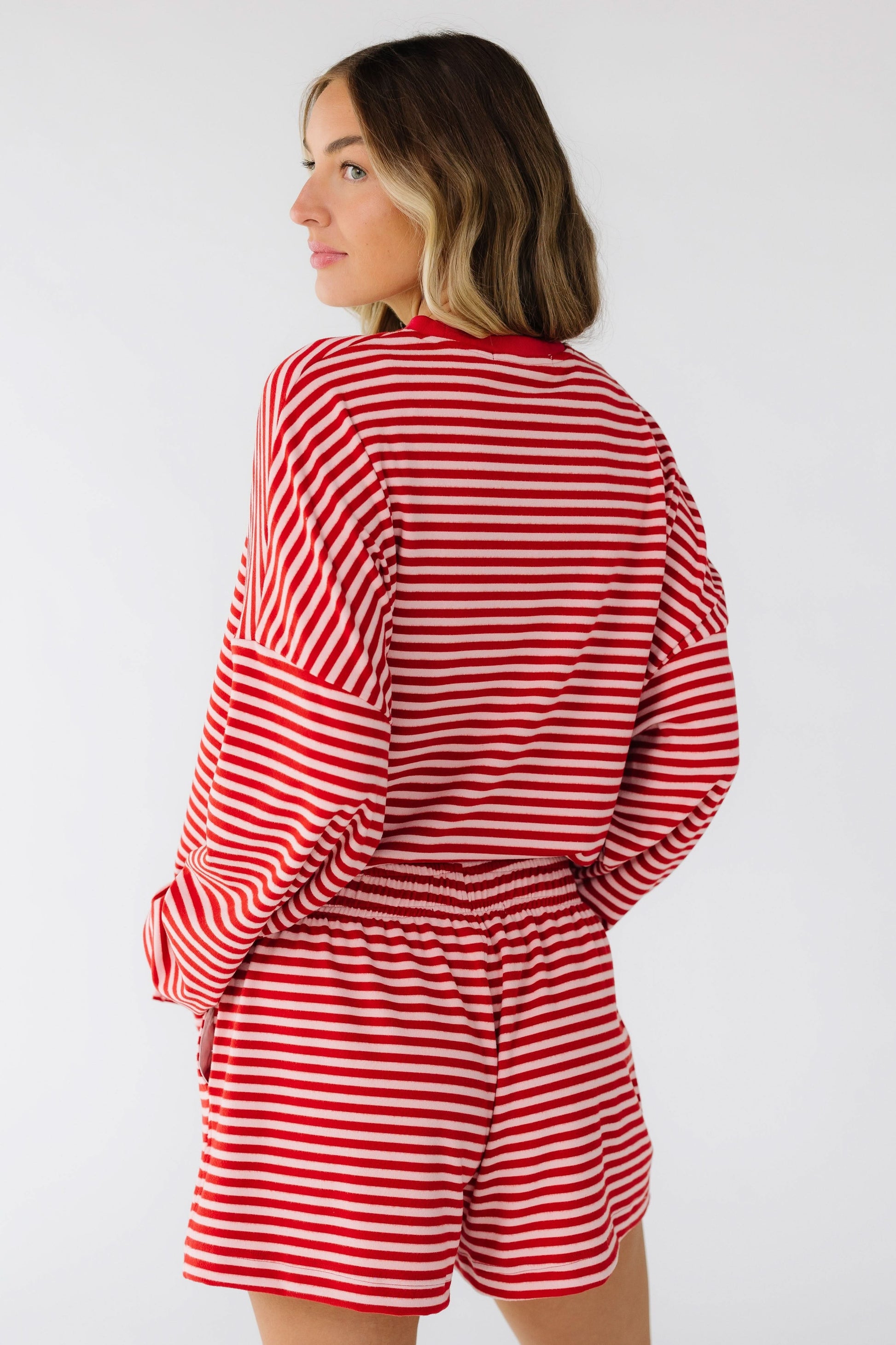 Back view of a woman wearing a red & pink stripe shorts set with long sleeves, and elastic waist shorts.