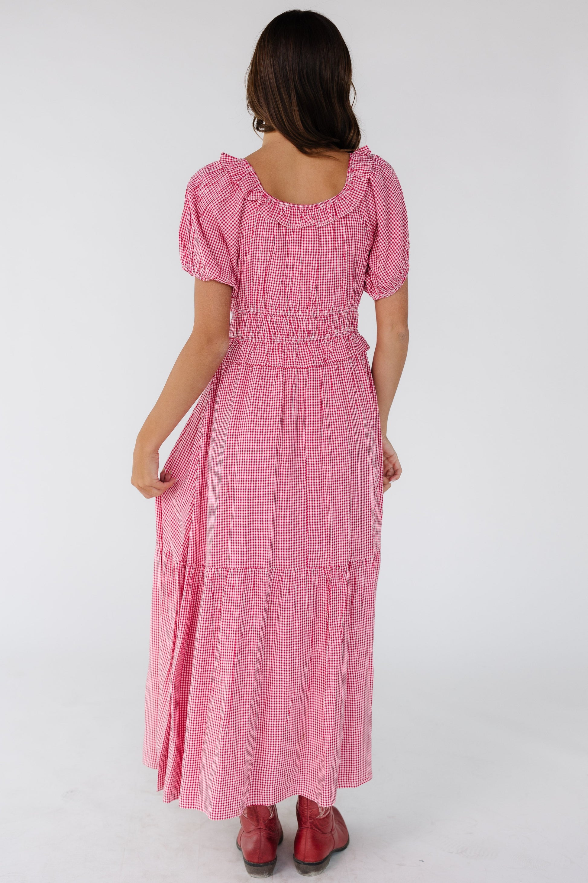 Back view of a woman wearing a red & white gingham with a back scoop neckline and a wide waistband and a wide bottom ruffle.