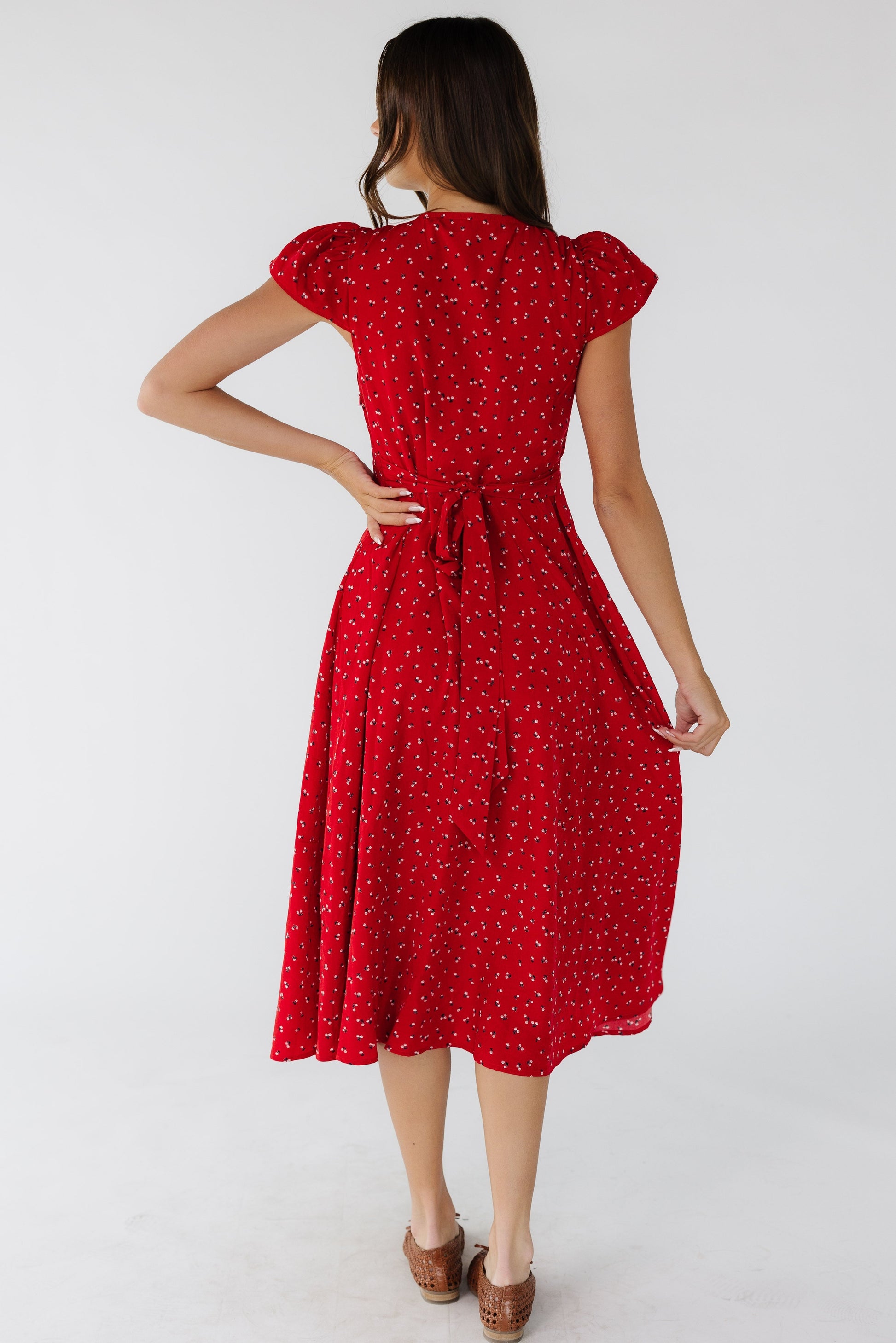 Back view of a young woman wearing a red floral midi dress with short flutter sleeve sand side ties.