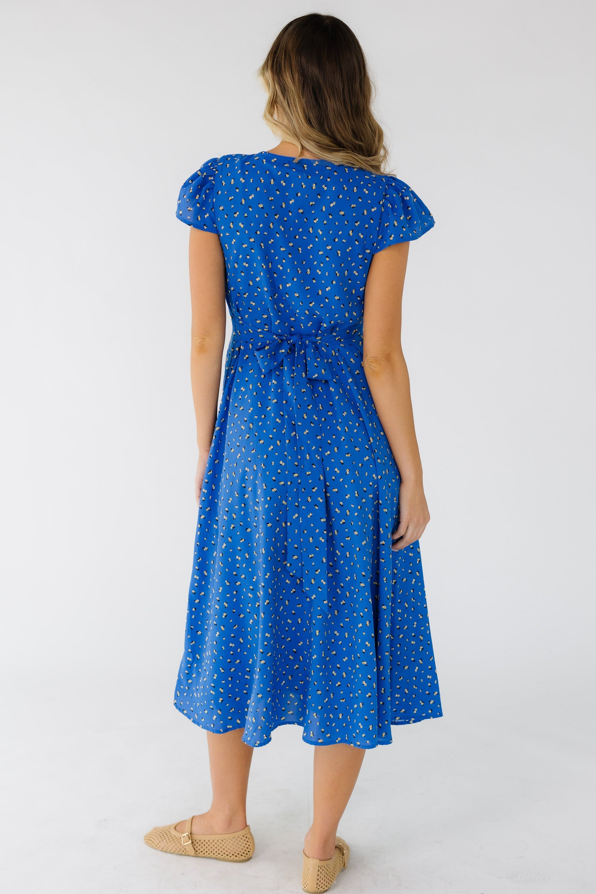 Back view of a woman wearing a blue floral midi dress with side ties, and flutter sleeves.