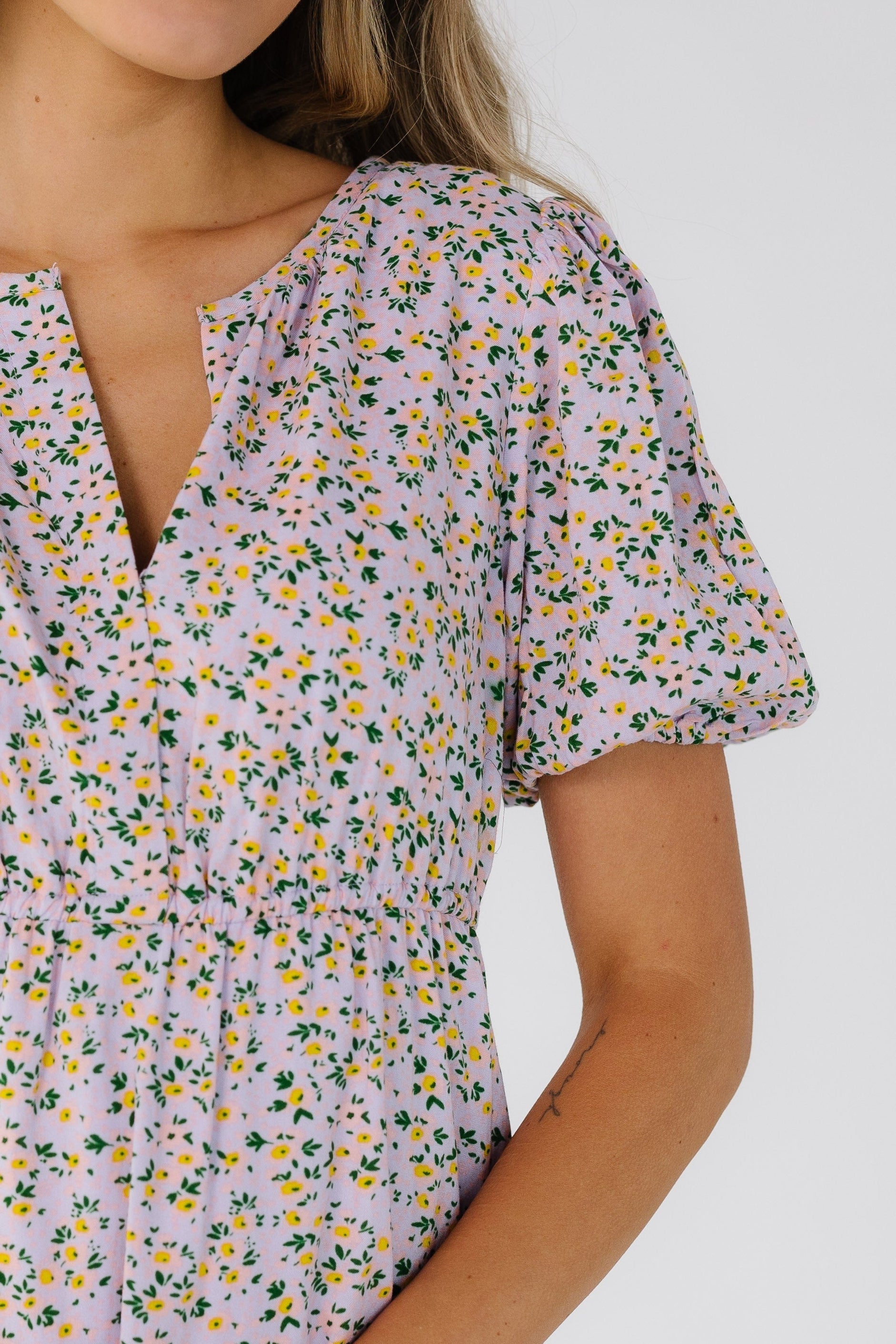 Close view of a woman wearing a light lavender floral dress with a V-neckline, short puff sleeves and an empire waist.