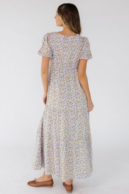 Back view of a woman wearing a lavender midi-maxi dress with puff sleeves, empire elastic waist and a loose tiered skirt.