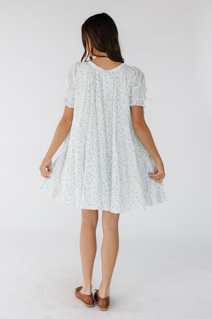 Back view of a young woman wearing a white & blue floral print short dress with short puff sleeves.